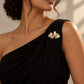 Tie Shop Gold Pleated Ribbon Brooch on black dress. بروش نسائي من تاي شوب بتصميم طيات ذهبية، إكسسوار أنيق للحجاب والملابس.