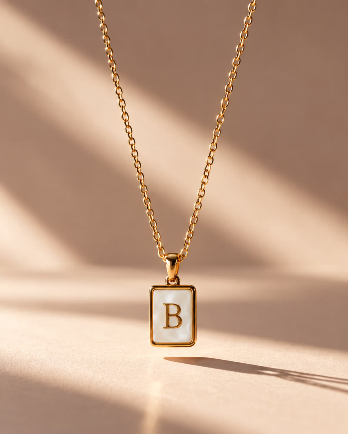 Tie Shop B Initial Necklace gold mother of pearl pendant display. سلاسل نسائية من تاى شوب بي إنيشال نيكليس، قلادة ذهبية بدلاية مستطيلة بحرف B وخلفية صدف عرق اللؤلؤ، مجوهرات وإكسسوارات أنيقة.