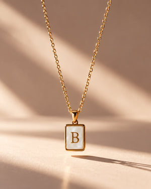 Tie Shop B Initial Necklace gold mother of pearl pendant display. سلاسل نسائية من تاى شوب بي إنيشال نيكليس، قلادة ذهبية بدلاية مستطيلة بحرف B وخلفية صدف عرق اللؤلؤ، مجوهرات وإكسسوارات أنيقة.