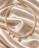 Tie Shop Moon & Star Necklace pearl beaded choker with gold celestial charms on silk background. سلاسل نسائية من تاى شوب مون آند ستار نيكليس، عقد من اللؤلؤ مزين بدلايات ذهبية على شكل هلال ونجمة مرصعة بالفصوص، مجوهرات وإكسسوارات أنيقة.