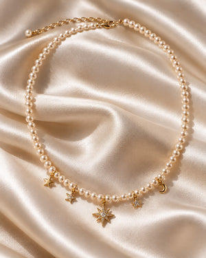 Tie Shop Moon & Star Necklace pearl beaded choker with gold celestial charms on silk background. سلاسل نسائية من تاى شوب مون آند ستار نيكليس، عقد من اللؤلؤ مزين بدلايات ذهبية على شكل هلال ونجمة مرصعة بالفصوص، مجوهرات وإكسسوارات أنيقة.