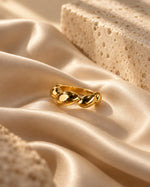 Tie Shop gold chunky croissant dome ring on smooth silk background. خواتم نسائية من تاي شوب خاتم كرواسون ذهبي بارز بتصميم كرويسانت دوم سميك، مجوهرات وإكسسوارات أنيقة.