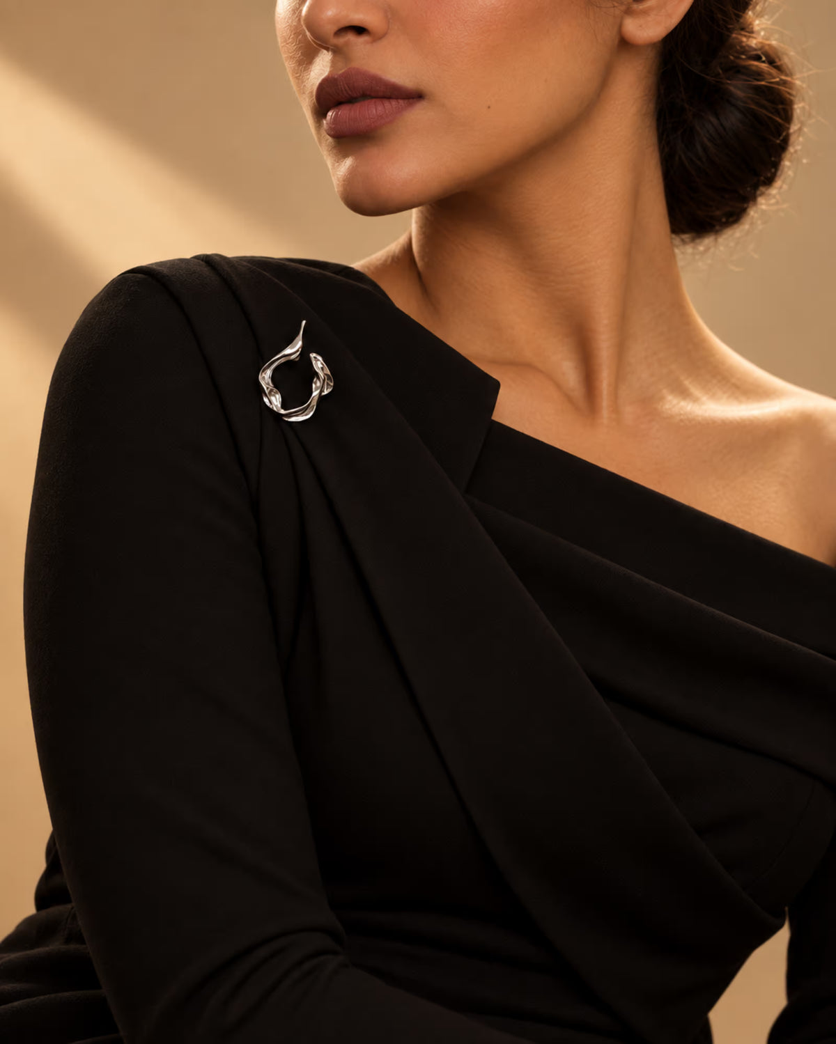 Model styling a black one-shoulder dress with the Abstract Fluid Silver Brooch from Tie Shop on the shoulder. موديل تنسق فستان أسود بكتف واحد مع بروش تجريدي انسيابي فضي من تاي شوب على الكتف.