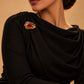 Model wearing a draped black formal dress styled with the Amber Stone Metallic Brooch from Tie Shop on the shoulder for special occasions. موديل ترتدي فستان سهرة أسود منسدل مزين بـ بروش بحجر عنبري إطار معدني من تاي شوب على الكتف للمناسبات.