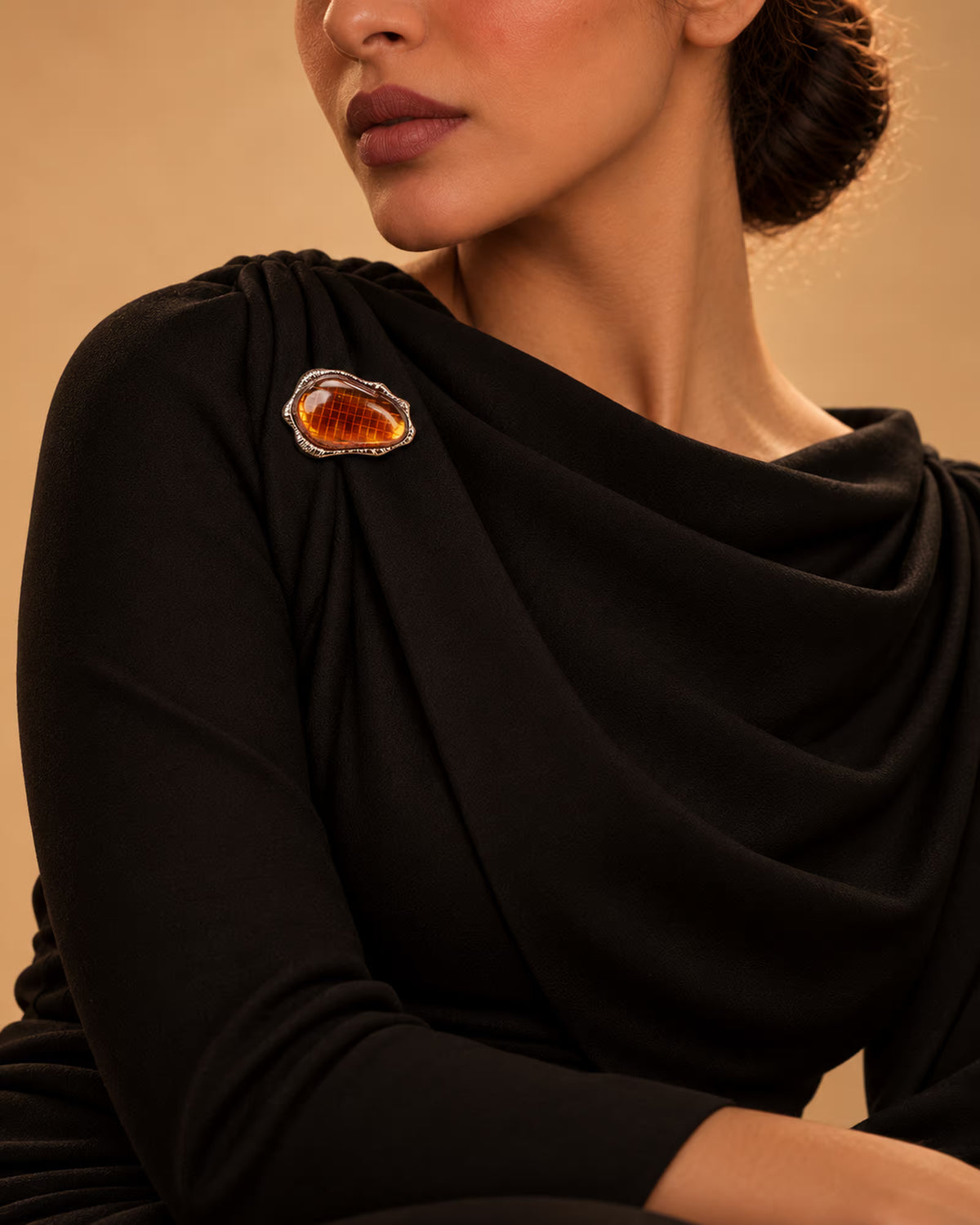 Model wearing a draped black formal dress styled with the Amber Stone Metallic Brooch from Tie Shop on the shoulder for special occasions. موديل ترتدي فستان سهرة أسود منسدل مزين بـ بروش بحجر عنبري إطار معدني من تاي شوب على الكتف للمناسبات.