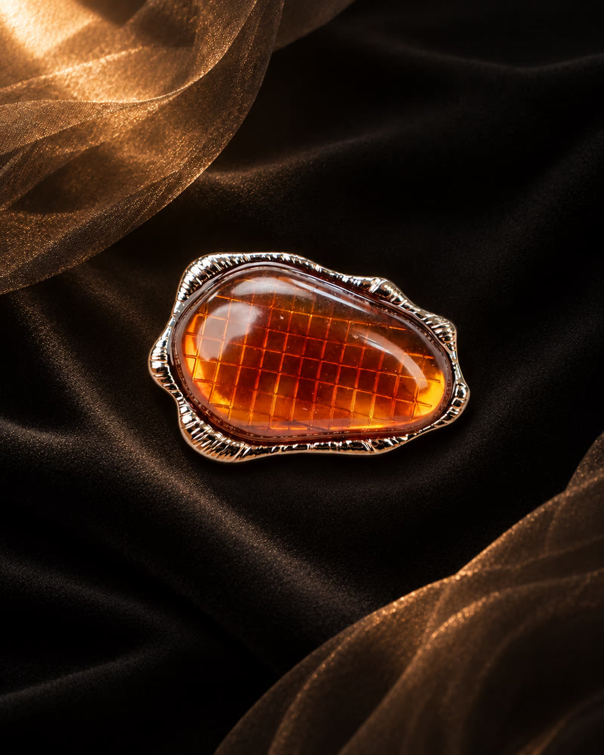 Close-up of Tie Shop Amber Stone Metallic Brooch featuring an amber-colored resin center with grid texture in a textured frame, suitable for abayas and dresses. صورة مقربة لـ بروش بحجر عنبري إطار معدني من تاي شوب بمركز راتنجي عسلي محفور بإطار مموج، مثالي للعبايات والفساتين.