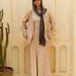 Woman in a beige outfit with a gray scarf standing against a light-colored wall.