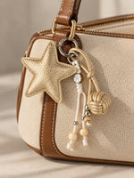 Tie Shop Beige Gold Leather Star Bag Charm on canvas purse. تعليقة حقيبة نسائية من تاي شوب بنجمة ذهبية وخرز، إكسسوار أنيق للشنط.