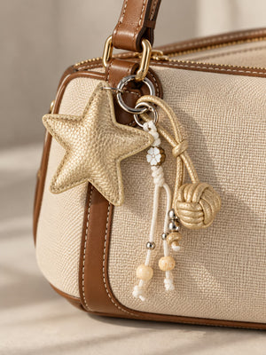 Tie Shop Beige Gold Leather Star Bag Charm on canvas purse. تعليقة حقيبة نسائية من تاي شوب بنجمة ذهبية وخرز، إكسسوار أنيق للشنط.