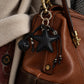 Tie Shop Black Leather Star Bag Charm on brown purse. تعليقة حقيبة نسائية من تاي شوب بنجمة جلد سوداء وكرة مجدولة، إكسسوار أنيق للشنط.