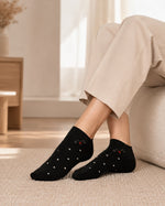 A person wearing black ankle socks with small white polka dots and a tiny red accent, paired with beige pants, sitting on a light-colored sofa in a bright, modern room.
