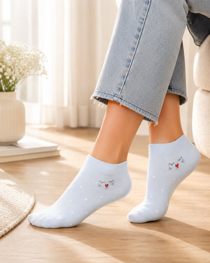 A person wearing light blue ankle socks with a small embroidered cat and red heart design, paired with light blue jeans in a bright indoor setting.