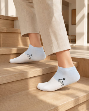 A person wearing light blue and white ankle socks with a small black graphic, standing on wooden stairs in a sunlit indoor setting.