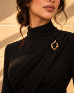 Model wearing a black turtleneck dress decorated with the Abstract Fluid Gold Brooch from Tie Shop for formal occasions. موديل ترتدي فستان أسود بياقة مرتفعة مزين بـ بروش تجريدي انسيابي ذهبي من تاي شوب للمناسبات.