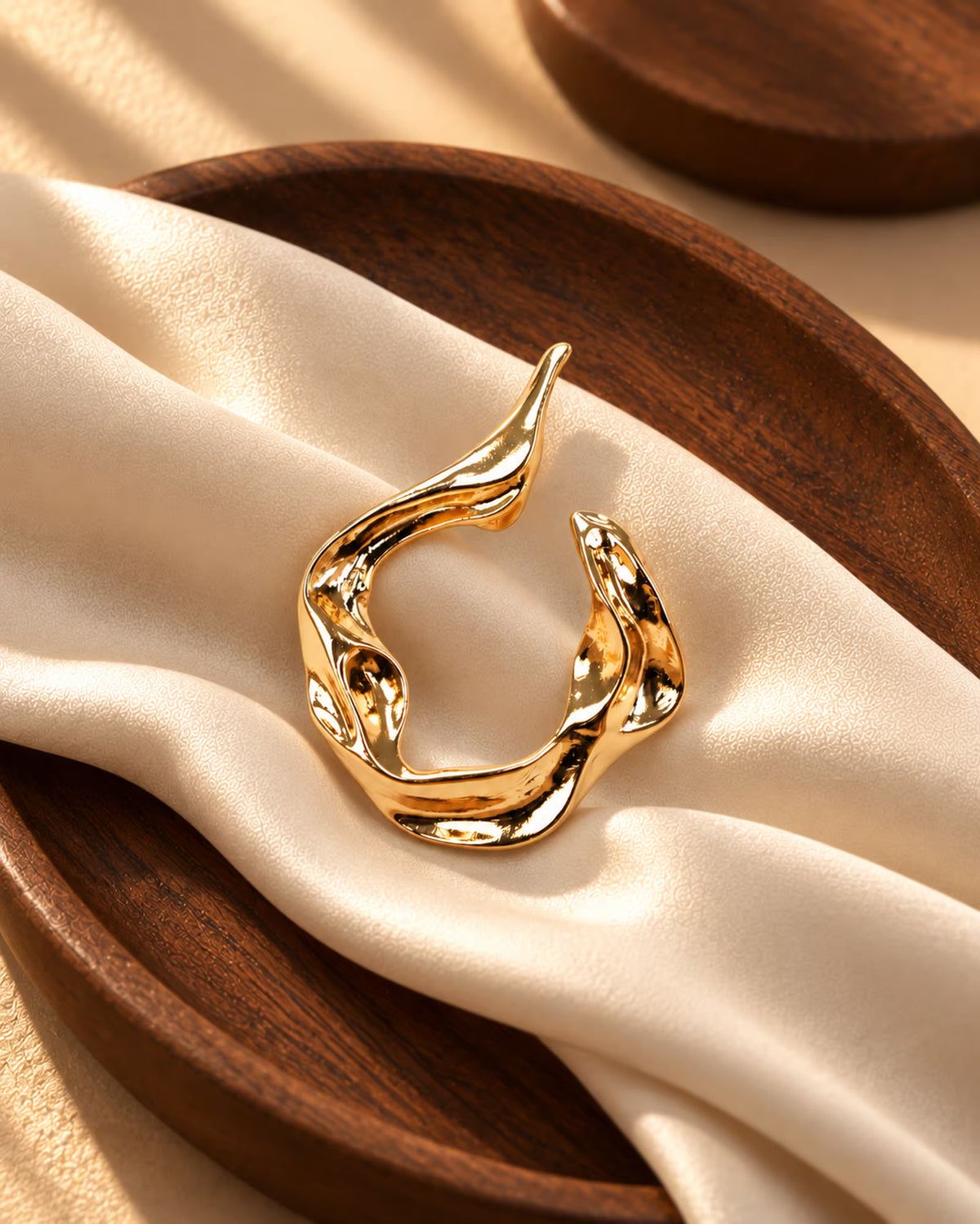 Close-up of Tie Shop Abstract Fluid Gold Brooch, a luxury metallic accessory for abayas, dresses, and hijabs. صورة مقربة لـ بروش تجريدي انسيابي ذهبي من تاي شوب، اكسسوار معدني فاخر للعبايات والفساتين والحجاب.