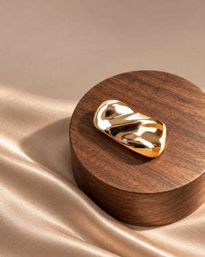 Tie Shop Gold Wave Bar Brooch on wooden pedestal. بروش نسائي من تاي شوب بلمسة ذهبية مصقولة ومطعجة، إكسسوار أنيق للحجاب والملابس.