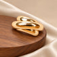 Tie Shop Gold Interlocking Curved Brooch on wooden base. بروش نسائي من تاي شوب بحلقات ذهبية ناعمة ومصقولة، إكسسوار أنيق للحجاب والملابس.
