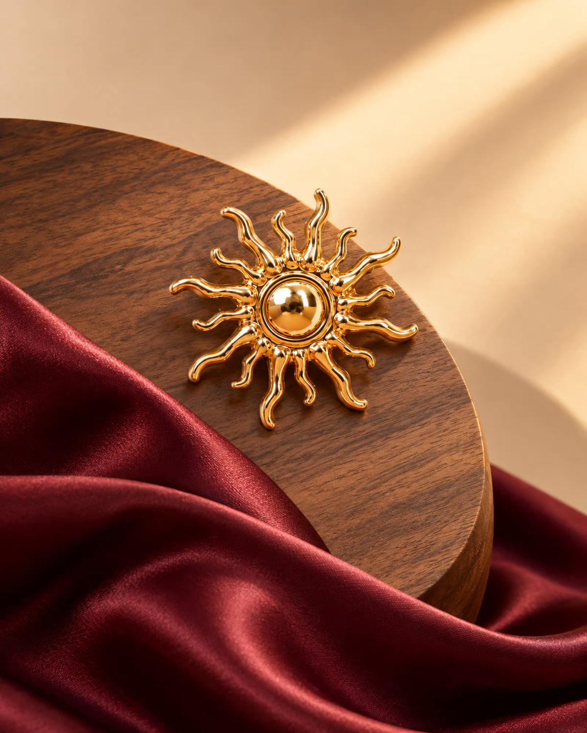 Tie Shop Gold Sunburst Brooch on wooden base with burgundy silk. بروش نسائي من تاي شوب بتصميم قرص الشمس الذهبي، إكسسوار أنيق للحجاب والملابس.