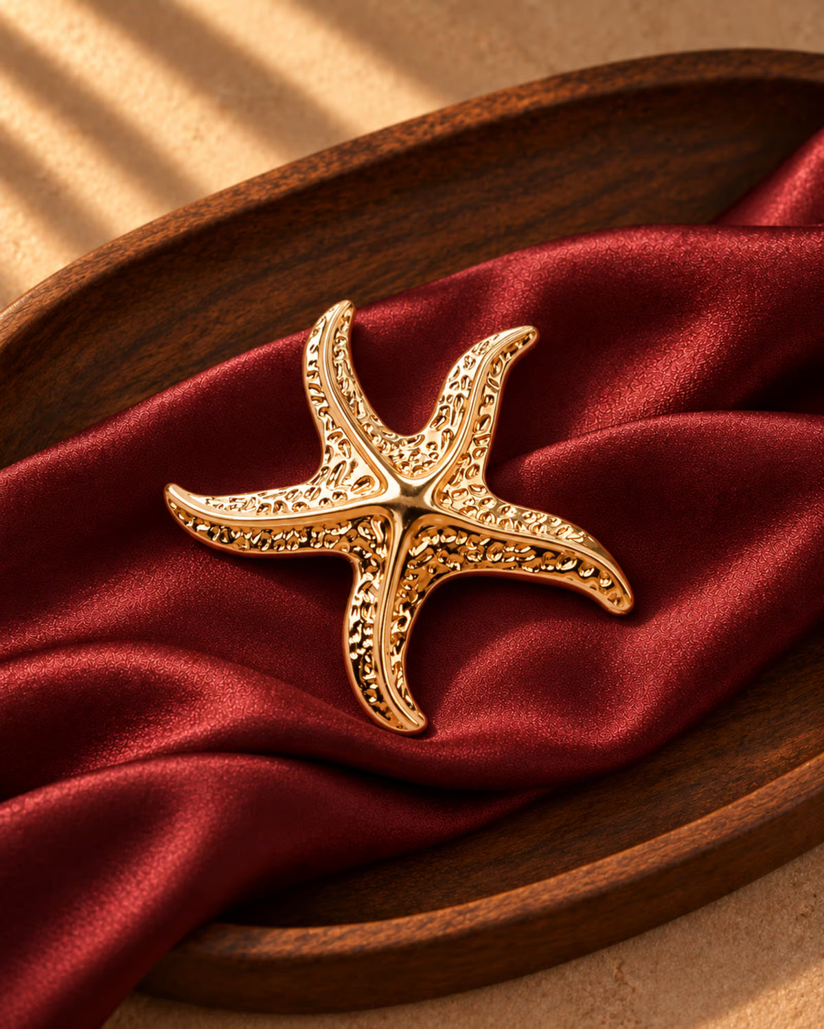Tie Shop Gold Starfish Brooch on burgundy satin. بروش نسائي من تاي شوب على شكل نجم بحر ذهبي، إكسسوار أنيق للحجاب والملابس.