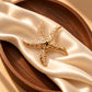 Tie Shop Gold Starfish Brooch on wooden pedestal. بروش نسائي من تاي شوب بتفاصيل محفورة باللون الذهبي، إكسسوار أنيق للحجاب والملابس.