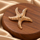 Tie Shop Gold Starfish Brooch on champagne satin. بروش نسائي من تاي شوب بلمسة ذهبية فاخرة، إكسسوار أنيق للحجاب والملابس.