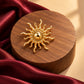 Close-up of Tie Shop Gold Sunburst Brooch on wooden pedestal. بروش نسائي من تاي شوب بتصميم شمس مصقولة، إكسسوار أنيق للحجاب والملابس.