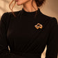 Model wearing an elegant draped black dress styled with Tie Shop Gold Crumpled Foil Brooch on the chest, a luxury fashion statement accessory. موديل ترتدي فستان أسود أنيق بياقة ثنيات مزين بـ بروش ذهبي مجعد ومطروق من تاي شوب، لمسة فنية وراقية للملابس اكتشفي أناقة بروش تاى شوب مع الحجاب والملابس