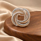Tie Shop Silver Interwoven Knot Brooch on wooden display. بروش نسائي من تاي شوب بتصميم حلقات فضية مضلعة، إكسسوار أنيق للحجاب والملابس.