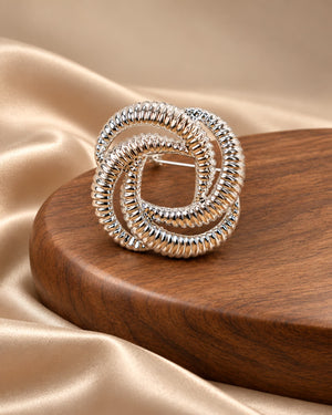 Tie Shop Silver Interwoven Knot Brooch on wooden display. بروش نسائي من تاي شوب بتصميم حلقات فضية مضلعة، إكسسوار أنيق للحجاب والملابس.