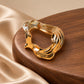 Tie Shop Gold Organic Curved Ring Brooch on wooden base. بروش نسائي من تاي شوب بخطوط مموجة ومصقولة، إكسسوار أنيق للحجاب والملابس.