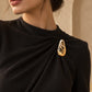 Model wearing an elegant black high-neck gown styled with Tie Shop Gold Textured Crystal Brooch on the chest, a luxury formal brooch. موديل ترتدي فستان أسود أنيق بياقة مرتفعة مزين بـ بروش ذهبي مموج مطعّم بالكريستال من تاي شوب، لمسة فخمة للملابس. اختاري بروش تاى شوب لتنسيق الحجاب والإطلالات