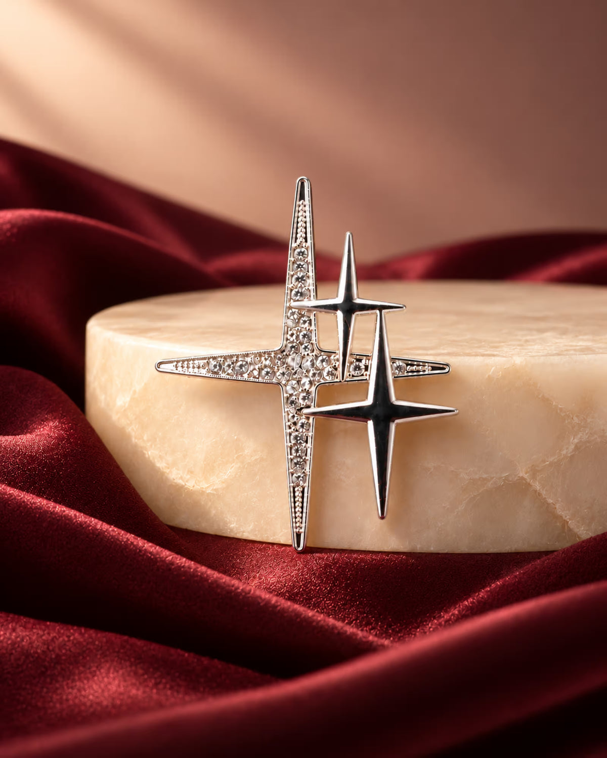 Close-up of Tie Shop Silver Sparkling Star Crystal Brooch on a marble pedestal with burgundy satin background, a premium fashion pin. صورة مقربة لـ بروش النجوم الفضي المرصع بالكريستال من تاي شوب على قاعدة رخامية وقماش نبيتي فاخر. بروش Zia لإطلالة أنيقة مع الحجاب