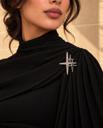 Model wearing an elegant black formal dress styled with Tie Shop Silver Sparkling Star Crystal Brooch on the shoulder, a luxurious metallic accessory. موديل ترتدي فستان أسود أنيق مزين بـ بروش النجوم الفضي المرصع بالكريستال من تاي شوب على الكتف، لمسة فاخرة للملابس.