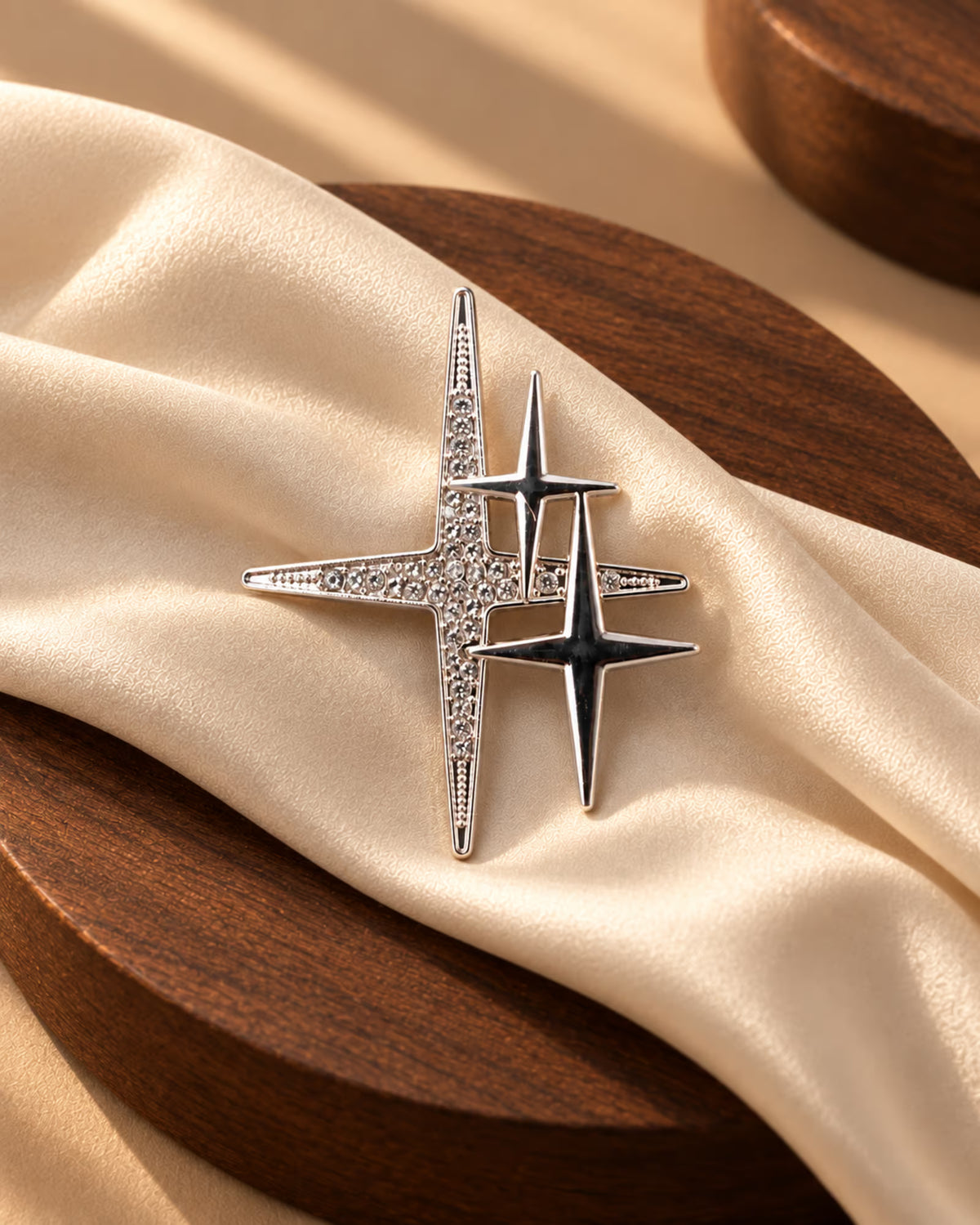 Close-up of Tie Shop Silver Sparkling Star Crystal Brooch on beige satin cloth and wooden plate, a stylish pin for abayas and hijabs. صورة مقربة لـ بروش النجوم الفضي المرصع بالكريستال من تاي شوب على قماش حرير بيج وطبق خشبي، دبوس أنيق للعبايات والحجاب.