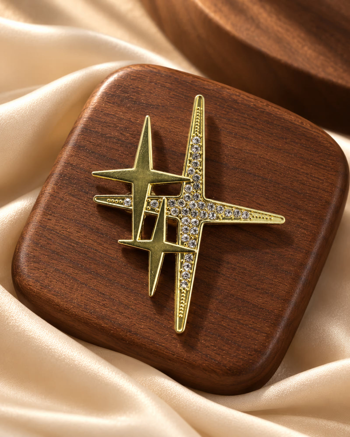 Close-up of Tie Shop Gold Sparkling Star Crystal Brooch on a wooden stand, an elegant metallic accessory with crystal embellishments. صورة مقربة لـ بروش النجوم الذهبي المرصع بالكريستال من تاي شوب على قاعدة خشبية، اكسسوار معدني راقي. مناسب للحجاب والملابس والمناسبات 