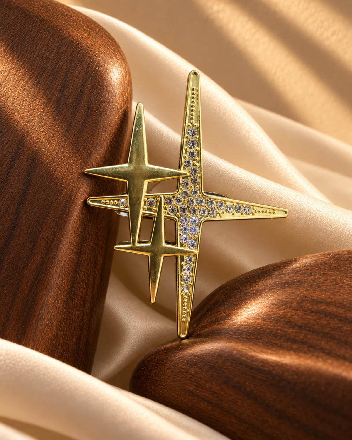 Detail shot of Tie Shop Gold Sparkling Star Crystal Brooch displayed between wooden props on silk fabric. صورة دقيقة لـ بروش النجوم الذهبي المرصع بالكريستال من تاي شوب بين عناصر خشبية وقماش حريري. بروش Zia النسائي، إكسسوار أنيق للحجاب والملابس
