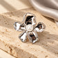 Close-up of Tie Shop Silver Calla Lily Pearl Flower Brooch on a stone surface with grey silk cloth, a stylish metallic accessory. صورة مقربة لـ بروش وردة اللؤلؤ الفضي من تاي شوب على سطح حجري مع قماش حرير رمادي، اكسسوار معدني جذاب. بروش للحجاب والملابس