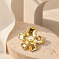 Close-up of Tie Shop Gold Calla Lily Pearl Flower Brooch with crystal accents on a stone pedestal, an elegant pin for abayas and dresses. صورة مقربة لـ بروش وردة اللؤلؤ الذهبي مع تفاصيل الكريستال من تاي شوب على قاعدة حجرية، دبوس أنيق للعبايات والفساتين.