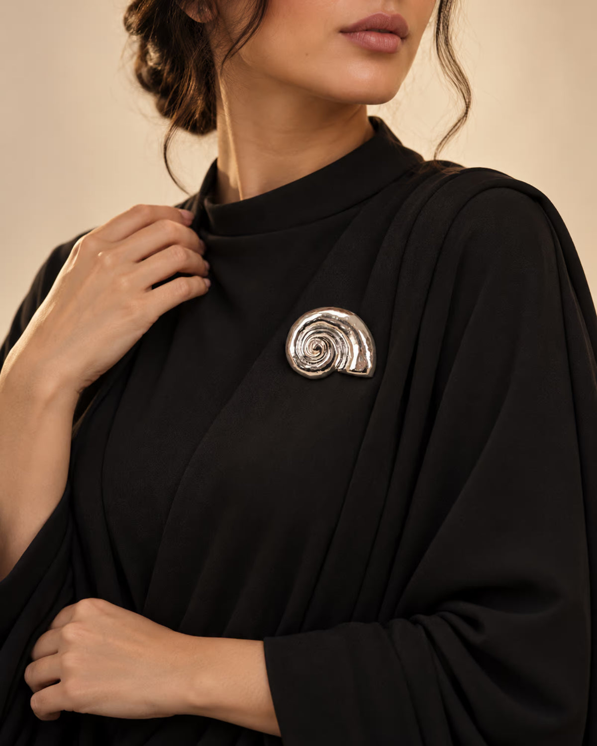 Model wearing an elegant black dress styled with Tie Shop Silver Polished Spiral Sea Shell Brooch, a chic metallic accessory for abayas and gowns. موديل ترتدي ملابس أنيقة باللون الأسود مزينة بـ بروش القوقعة المصقولة الفضي من تاي شوب،  اكسسوار راقي للعبايات والفساتين والطرح و الملابس