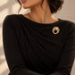 Model wearing a classic black dress styled with Tie Shop Gold Textured Hammered Circle Brooch on the chest, an elegant statement accessory for women. موديل ترتدي فستان أسود أنيق مزين بـ بروش دائري ذهبي مموج ومطروق من تاي  و شوب، اكسسوار راقي وعصري للملابس وللحجاب