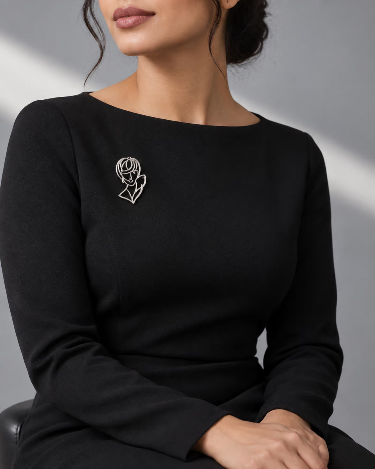 Model wearing an elegant black formal dress styled with Tie Shop Silver Abstract Line Art Face Brooch on the chest, a modern artistic accessory. موديل ترتدي فستان أسود أنيق مزين بـ بروش وجه المرأة الفني الفضي من تاي شوب على الصدر، لمسة فنية معاصرة للملابس. نسّقي إطلالتك مع بروش تاى شوب الأنيق