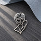 Close-up of Tie Shop Silver Abstract Line Art Face Brooch on a dark textured background with grey felt, a unique aesthetic pin. صورة مقربة لـ بروش وجه المرأة الفني الفضي من تاي شوب على خلفية رمادية، دبوس معدني بتصميم عصري. البروش النسائي من تاى شوب