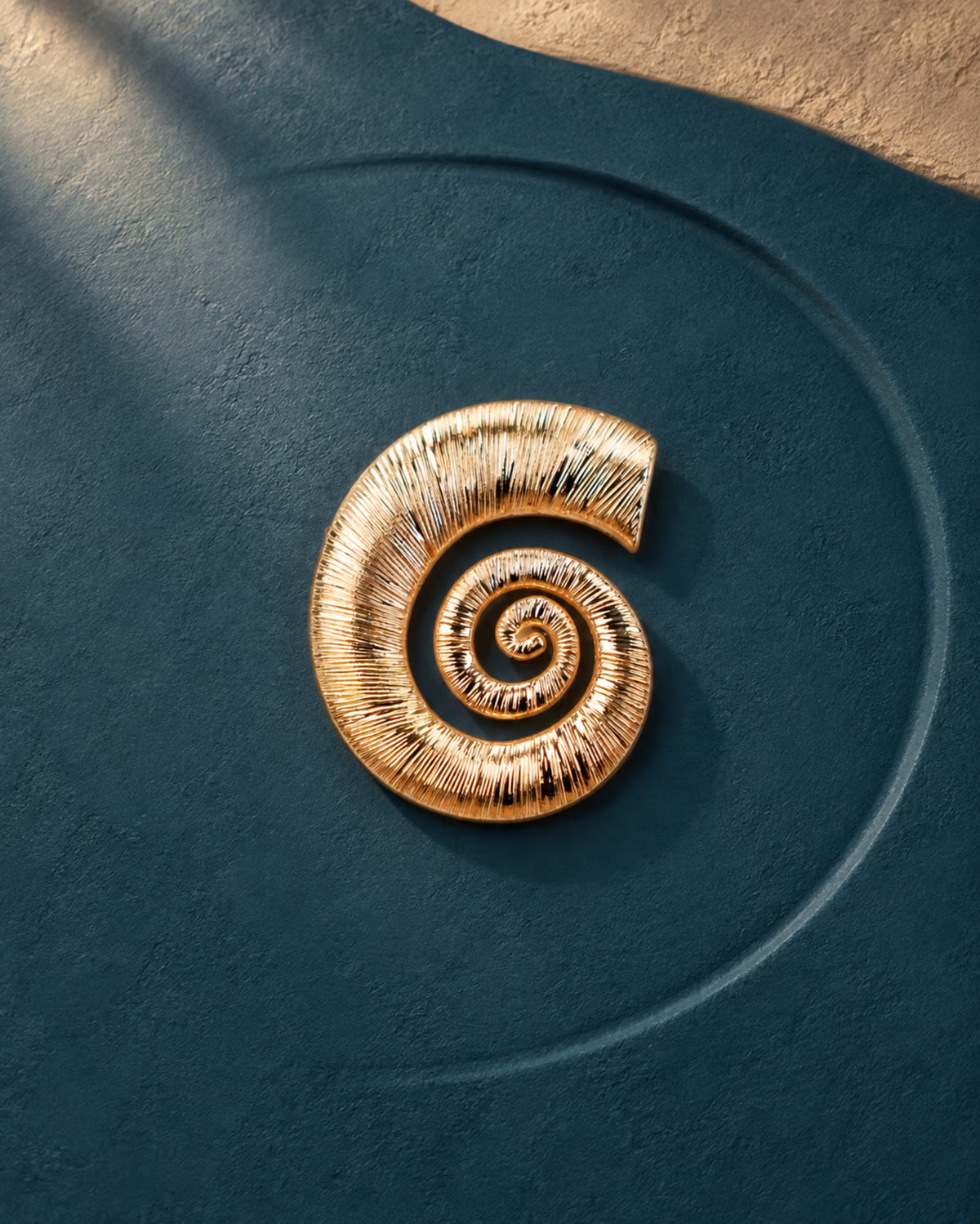 Close-up of Tie Shop Gold Swirl Nautilus Textured Brooch on a dark blue background, an elegant metallic accessory for abayas and dresses. صورة مقربة لـ بروش ذهبي بتصميم الحلزون المموج من تاي شوب على خلفية كحلية، اكسسوار معدني أنيق للعبايات والفساتين.