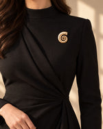 Model wearing an elegant black dress styled with Tie Shop Gold Swirl Nautilus Textured Brooch on the chest, a chic statement accessory. موديل ترتدي فستان أسود أنيق مزين بـ بروش ذهبي بتصميم الحلزون المموج من تاي شوب، لمسة راقية للملابس.