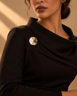 Model wearing a black formal dress decorated with the Textured Sunburst Round Gold Brooch from Tie Shop for special occasions. موديل ترتدي فستان سهرة أسود مزين بـ بروش ذهبي دائري بتصميم شعاعي من تاي شوب للمناسبات.