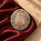 Close-up of Tie Shop Vintage Oval Textured Brooch with golden hammered frame and center stone on burgundy satin, an elegant accessory for abayas and dresses. صورة مقربة لـ بروش بيضاوي بتصميم ريترو محفور بلون ذهبي من تاي شوب على قماش ستان نبيتي، اكسسوار راقي للعبايات والفساتين.