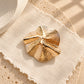Top-angle shot of Tie Shop Sculptural Shell Gold Brooch with spiral texture, ideal for elevating evening attire. صورة علوية لـ بروش ذهبي بتصميم صدفة تجريدية من تاي شوب بملمس مموج حلزوني، مثالي لإضفاء لمسة راقية على إطلالات المناسبات.