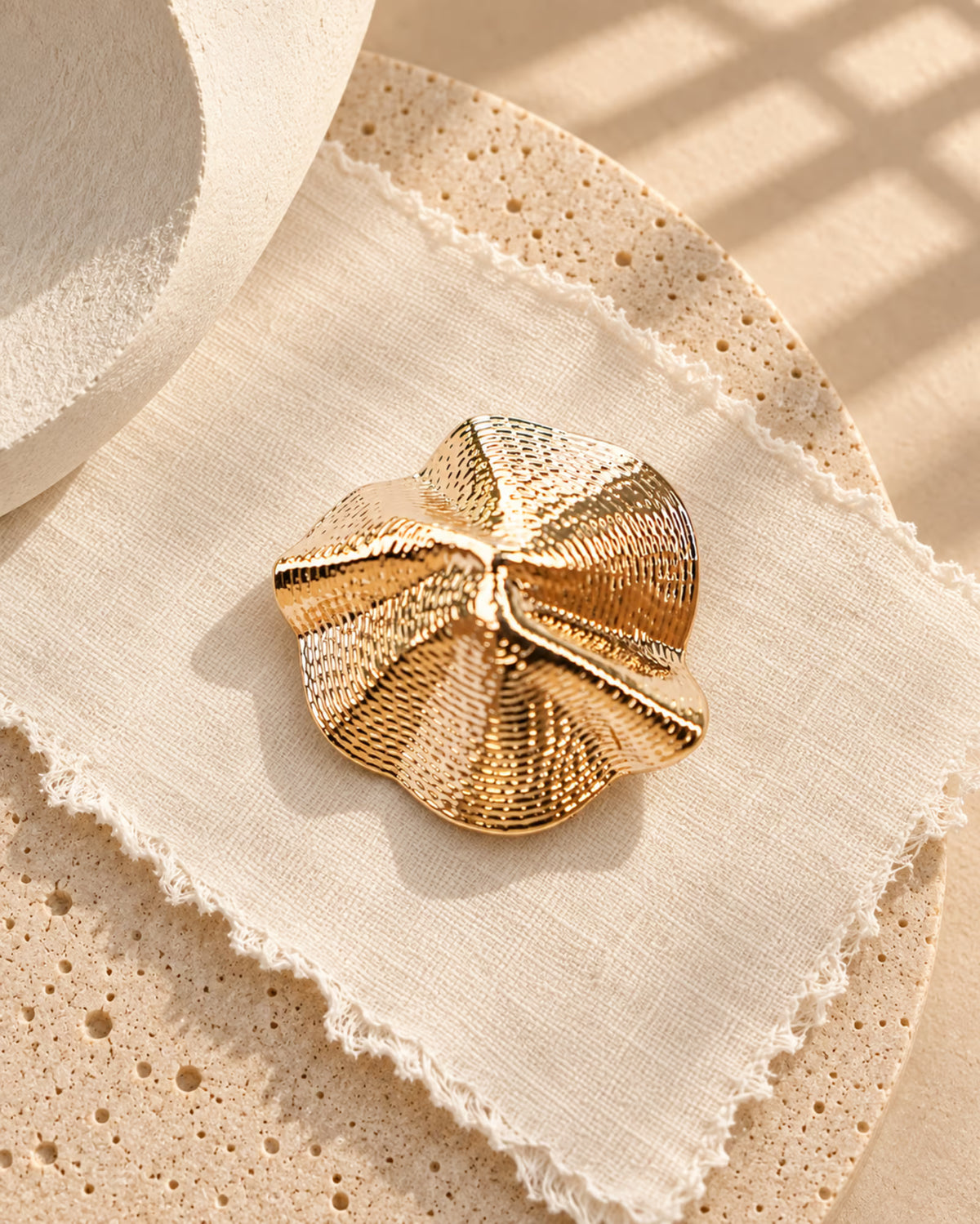 Top-angle shot of Tie Shop Sculptural Shell Gold Brooch with spiral texture, ideal for elevating evening attire. صورة علوية لـ بروش ذهبي بتصميم صدفة تجريدية من تاي شوب بملمس مموج حلزوني، مثالي لإضفاء لمسة راقية على إطلالات المناسبات.