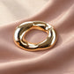 Detail shot of Tie Shop Chunky Gold Organic Ring Brooch displayed on soft dusty pink draped fabric, an elegant women's accessory. صورة دقيقة لـ بروش سميك ذهبي بتصميم حلقة عضوية مموجة من تاي شوب على قماش وردي ناعم، اكسسوار نسائي أنيق.