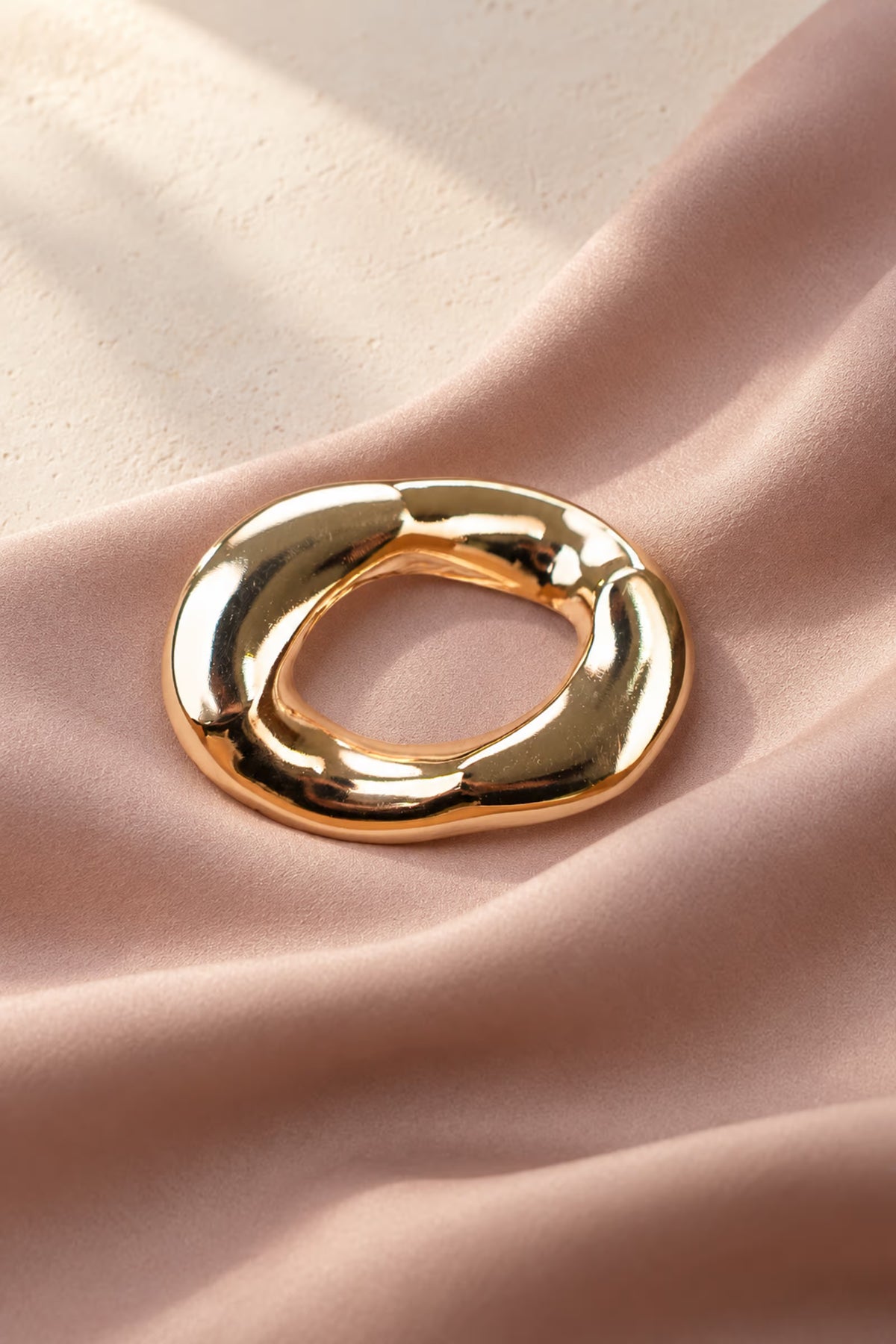 Detail shot of Tie Shop Chunky Gold Organic Ring Brooch displayed on soft dusty pink draped fabric, an elegant women's accessory. صورة دقيقة لـ بروش سميك ذهبي بتصميم حلقة عضوية مموجة من تاي شوب على قماش وردي ناعم، اكسسوار نسائي أنيق.